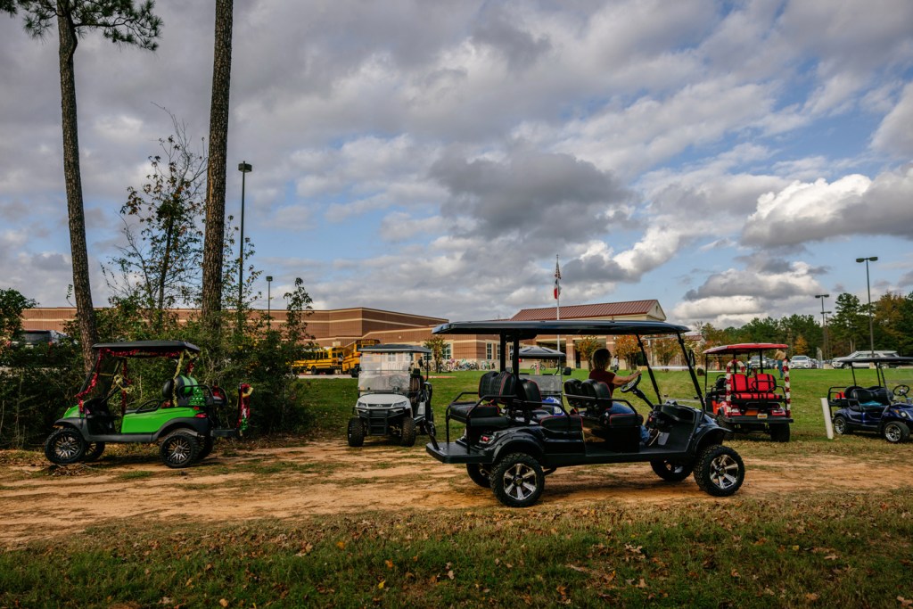 A golf cart drives by a row of other golf carts parked near Stewart Elementary School
