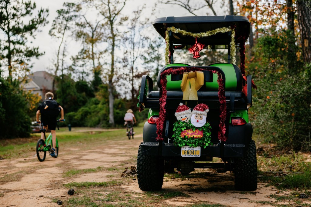 Children ride their bicycles by a decorated golf cart.