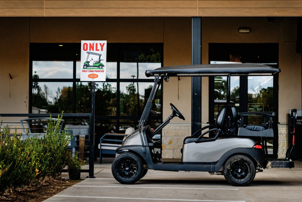 A golf cart is parked at a designated parking space for golf carts in front of a supermarket