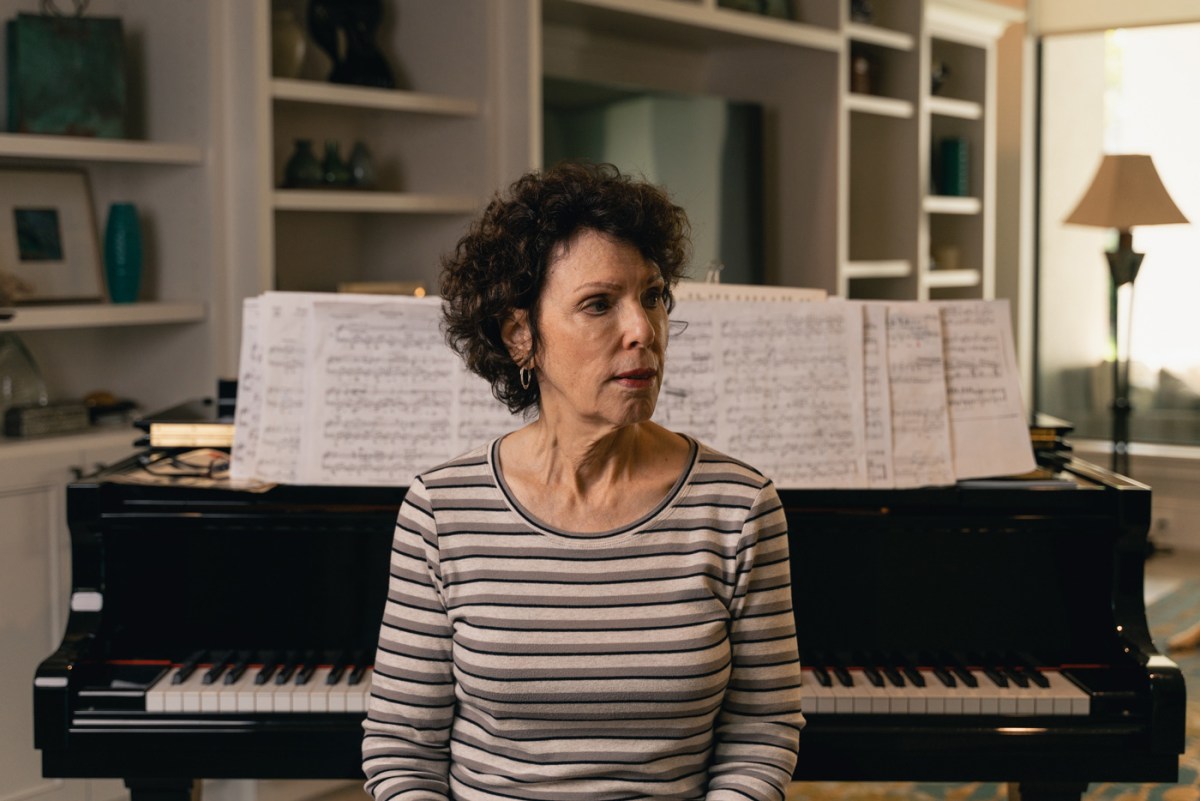 Bev Edelman sits by a piano looking away.