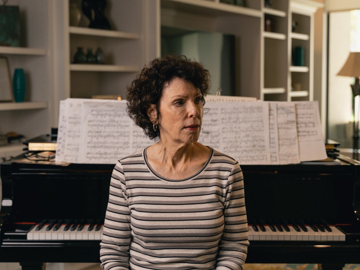 Bev Edelman sits by a piano looking away.