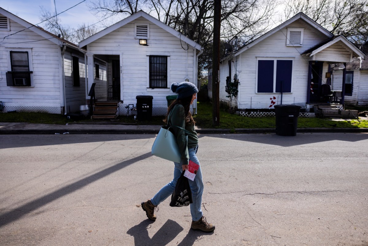 A woman walks in front of row houses carrying grocery bags.