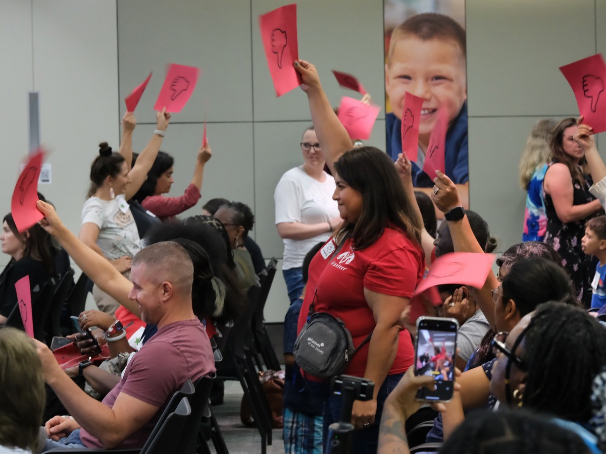 Community members attending Houston ISD's school board meeting stand and hold ‘thumbs down” signage in opposition to Superintendent Mike Miles' plans