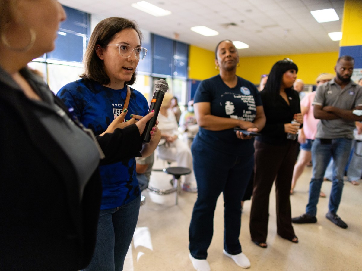 A school teacher speaks to a microphone during a town hall meeting at a school.