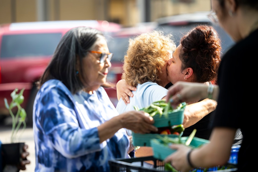 Rachel Flores, center, gets a hug and kiss from her granddaughter Gaby Gonzalez during a farmers market