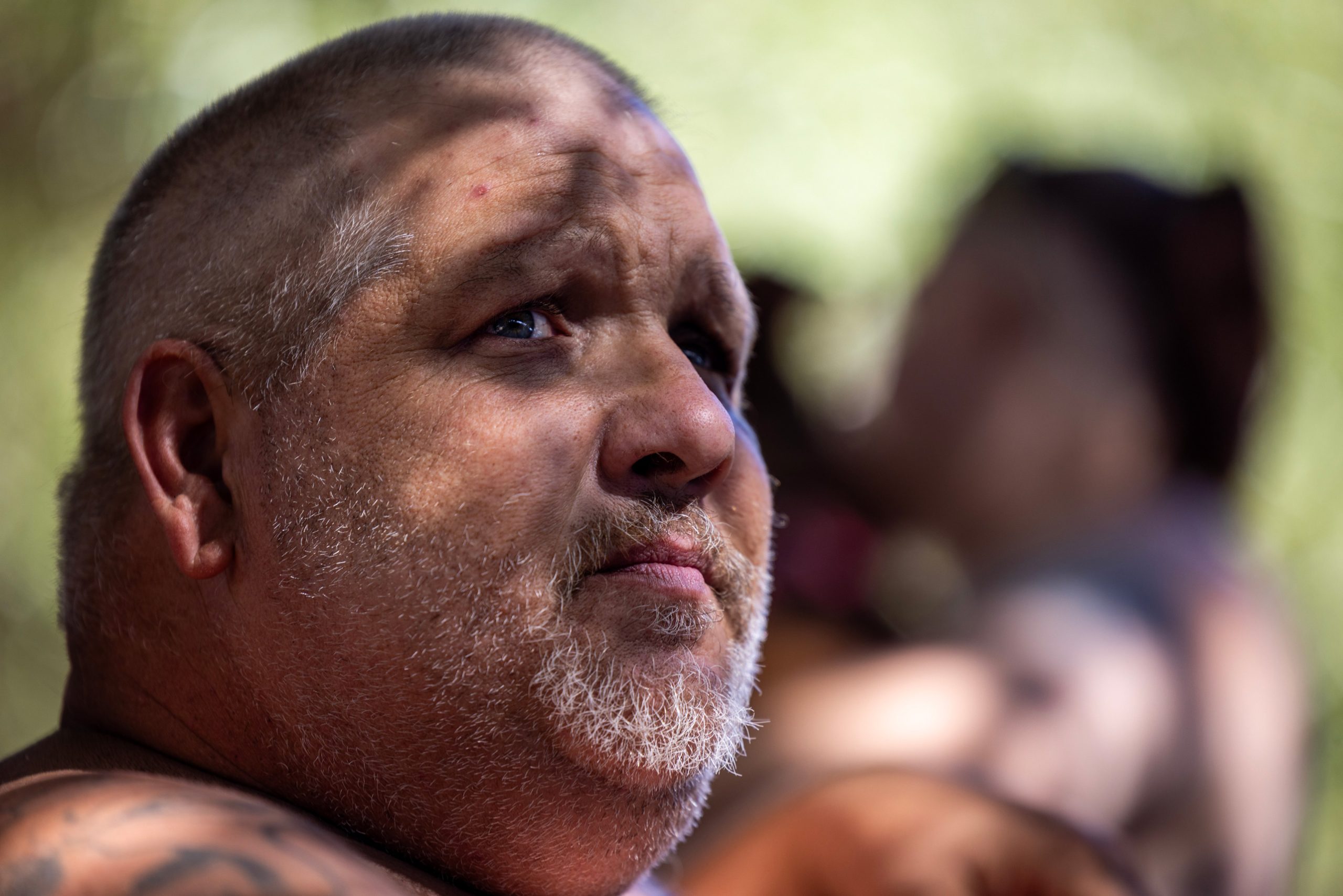 Tim Barnes looks off as he sits with family in an encampment under an overpass