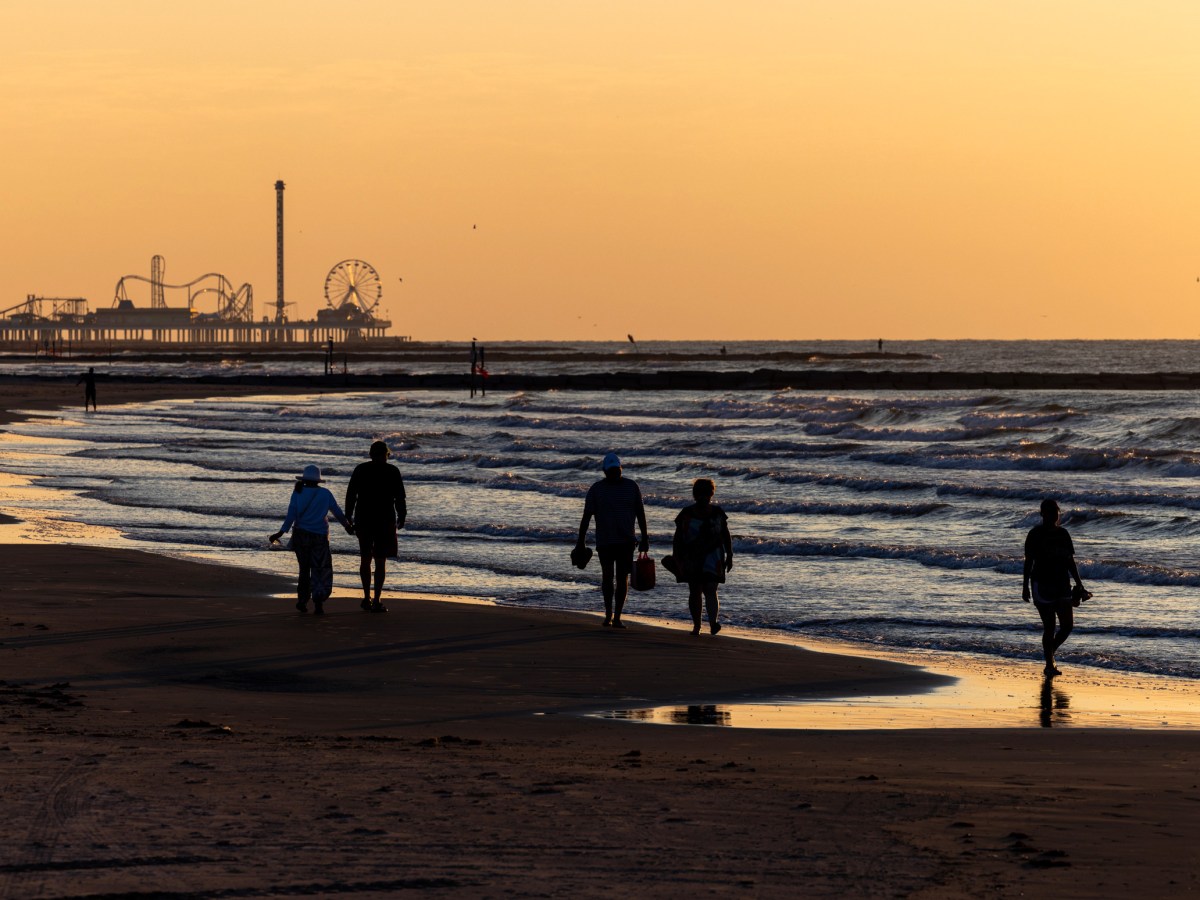 People walk along the shoreline during sunrise at Galveston Beach in Texas
