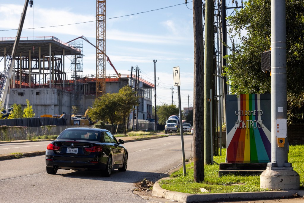 Cars pass by a utility box with Welcome to Montrose painted on it on the corner of Montrose Boulevard and Allen Parkway