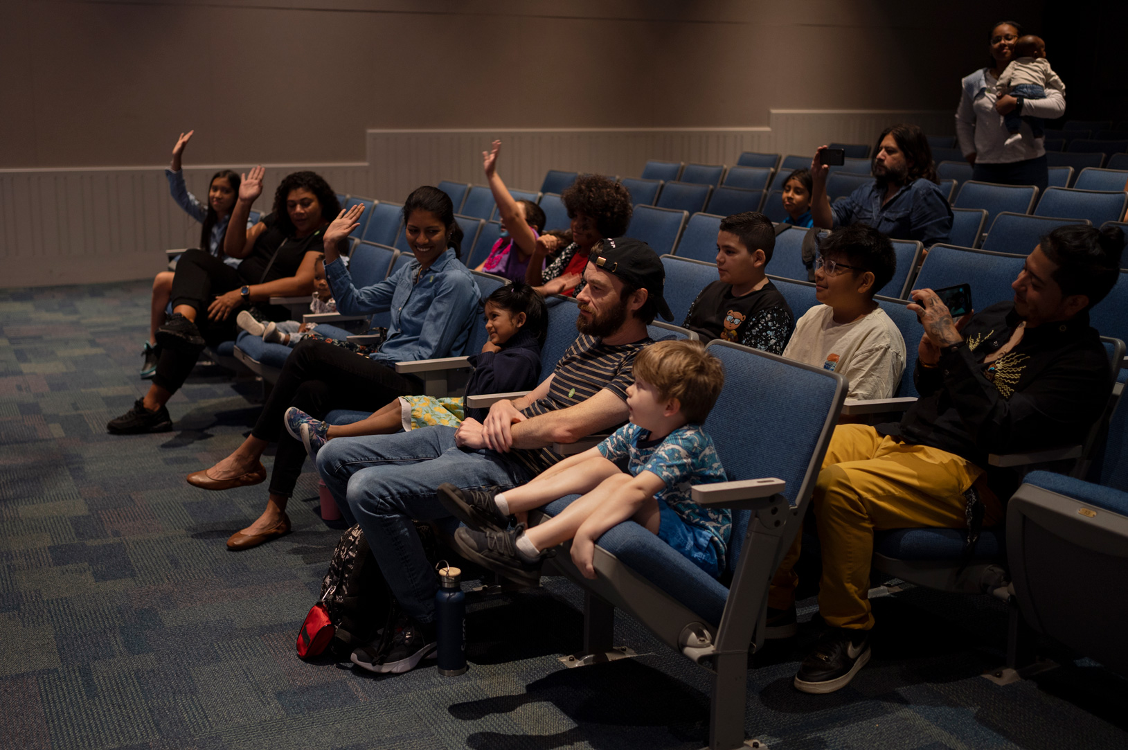 Children and parents raise their hands during Native American story time during the Indigenous People's Day celebration at the Children’s Museum Houston.