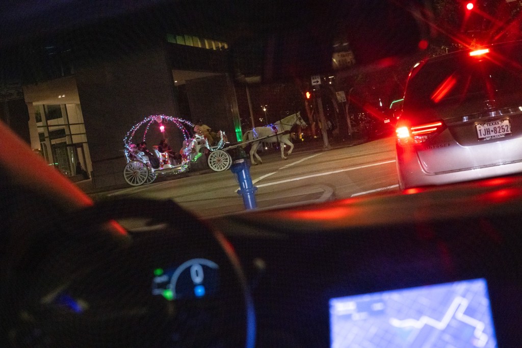 A horse-drawn carriage passes by as a Cruise vehicle waits at a stop light during a ride through downtown Houston 