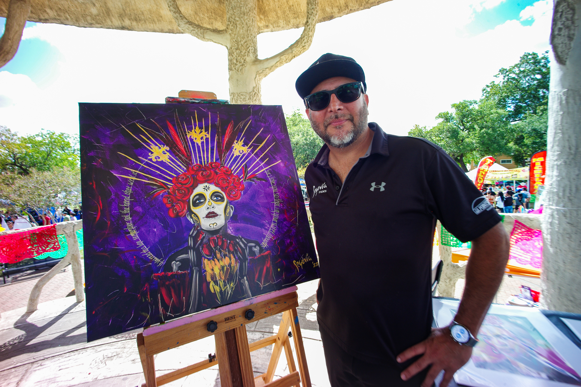 John Segovia stands with one of his paintings in the gazebo at Hidalgo Park, Saturday, Oct. 28, 2023, in Houston. Segovia was the featured artist for the Dia de los Muertos festival this year.