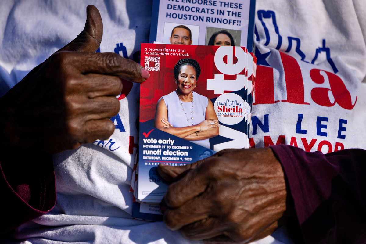 Voter holds election candidate promotional flyers near a polling site. On the promotional flyer, a photo of Congresswoman Sheila Jackson Lee is featured as well as other candidates.