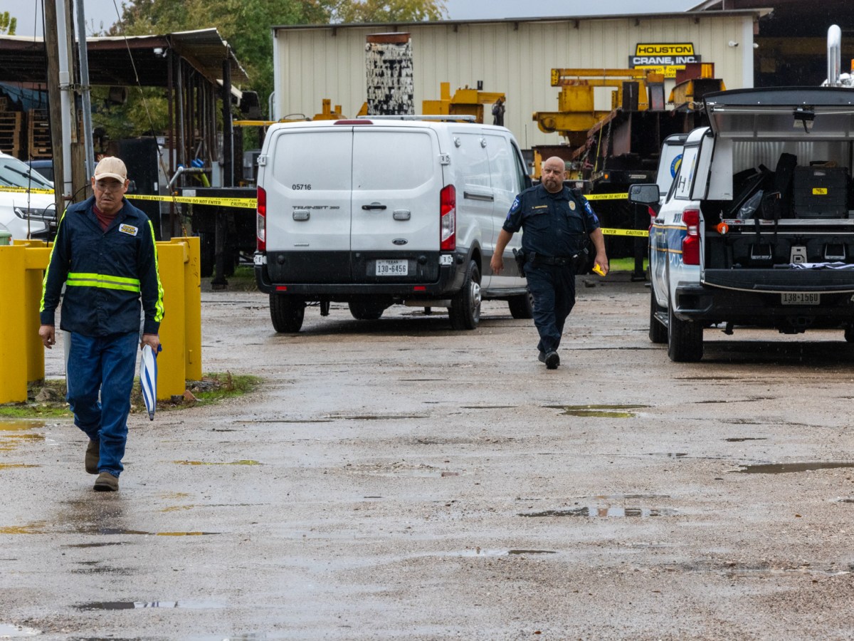 An officer and employee walk out of the back of Houston Crane, Inc. where a man was shot by police after a string of carjackings.