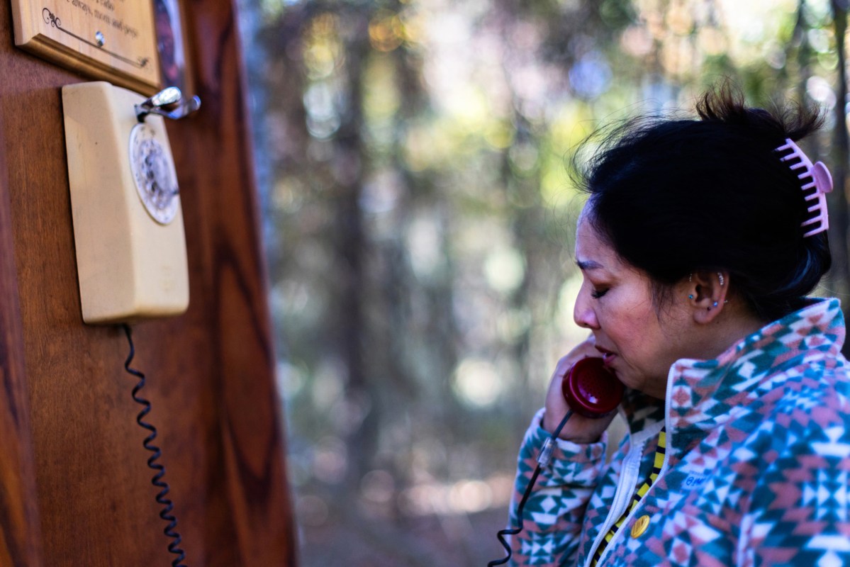 Nikki Revils closes her eyes as she picks up a red rotary phone receiver and places it to her ear, Wednesday, Dec. 6, 2023, in Houston. The wind phone in Cypress placed at Russ Poppe Family Park is one of more than a hundred around the nation and world that help mourners bridge the gap between the living and the dead.