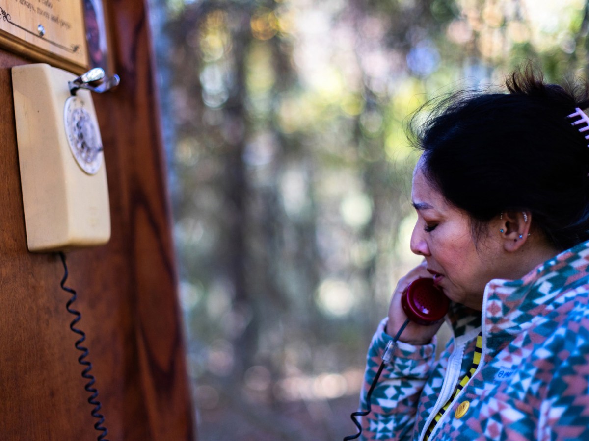 Nikki Revils closes her eyes as she picks up a red rotary phone receiver and places it to her ear, Wednesday, Dec. 6, 2023, in Houston. The wind phone in Cypress placed at Russ Poppe Family Park is one of more than a hundred around the nation and world that help mourners bridge the gap between the living and the dead.