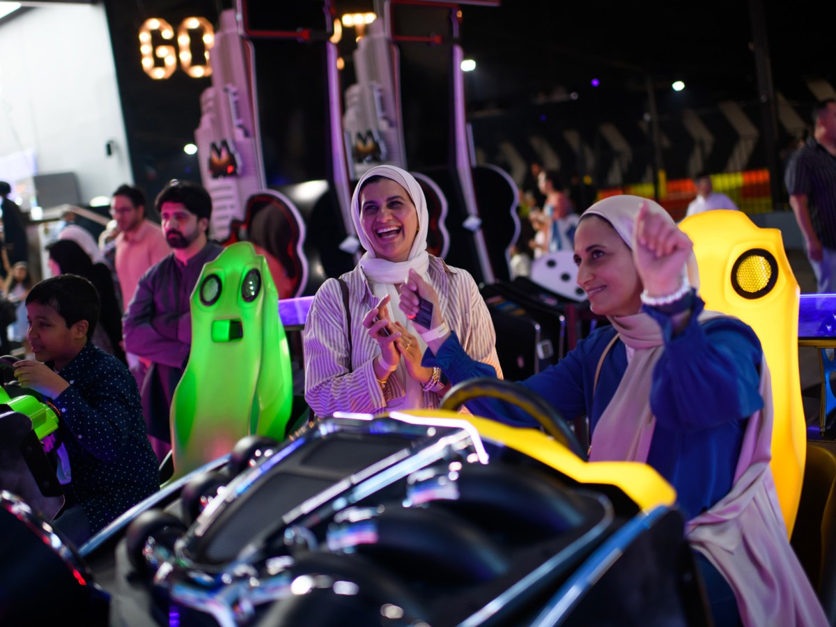 Nadiah Ammar (center) celebrates with her sister Yasmina Ammar (left) after driving a race car during an arcade game at an Eid celebration held by the Clear Lake Islamic Center at Marquee at the Mainland