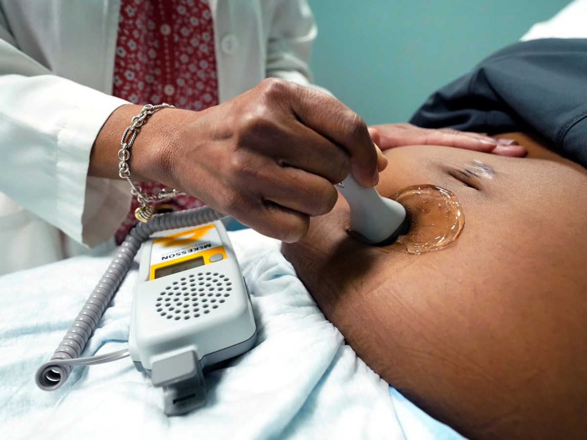 A doctor uses a hand-held Doppler probe on a pregnant woman to measure the heartbeat of the fetus