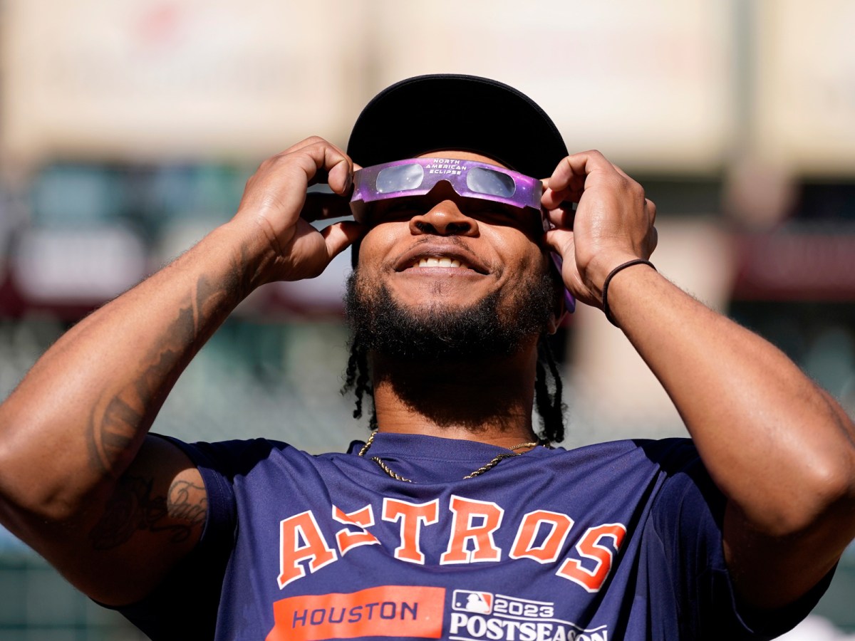 Houston Astros outfielder Corey Julks uses protective glasses to look at the solar eclipse during baseball practice in Houston, Saturday, Oct. 14, 2023.