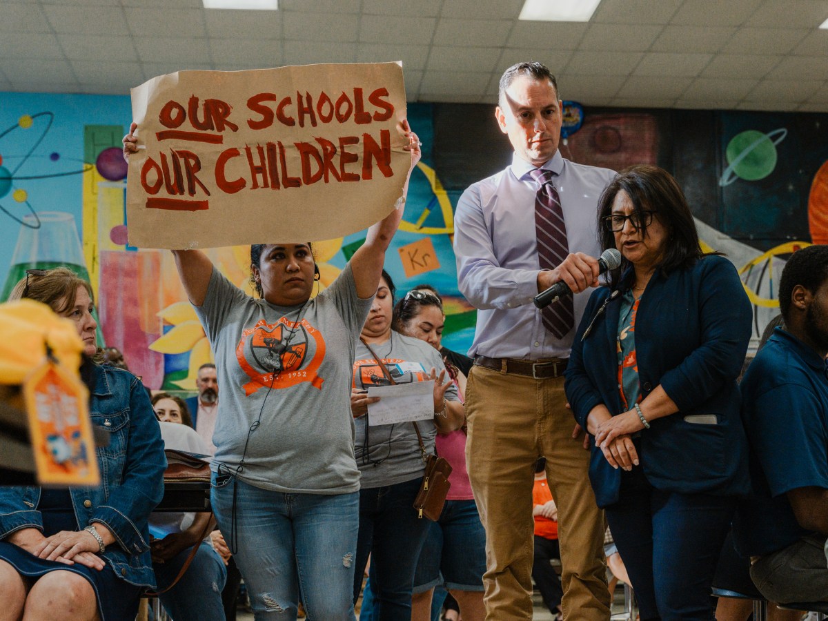 Celina Manzano holds a sign as a translator recites her question to Houston ISD Superintendent Mike Miles