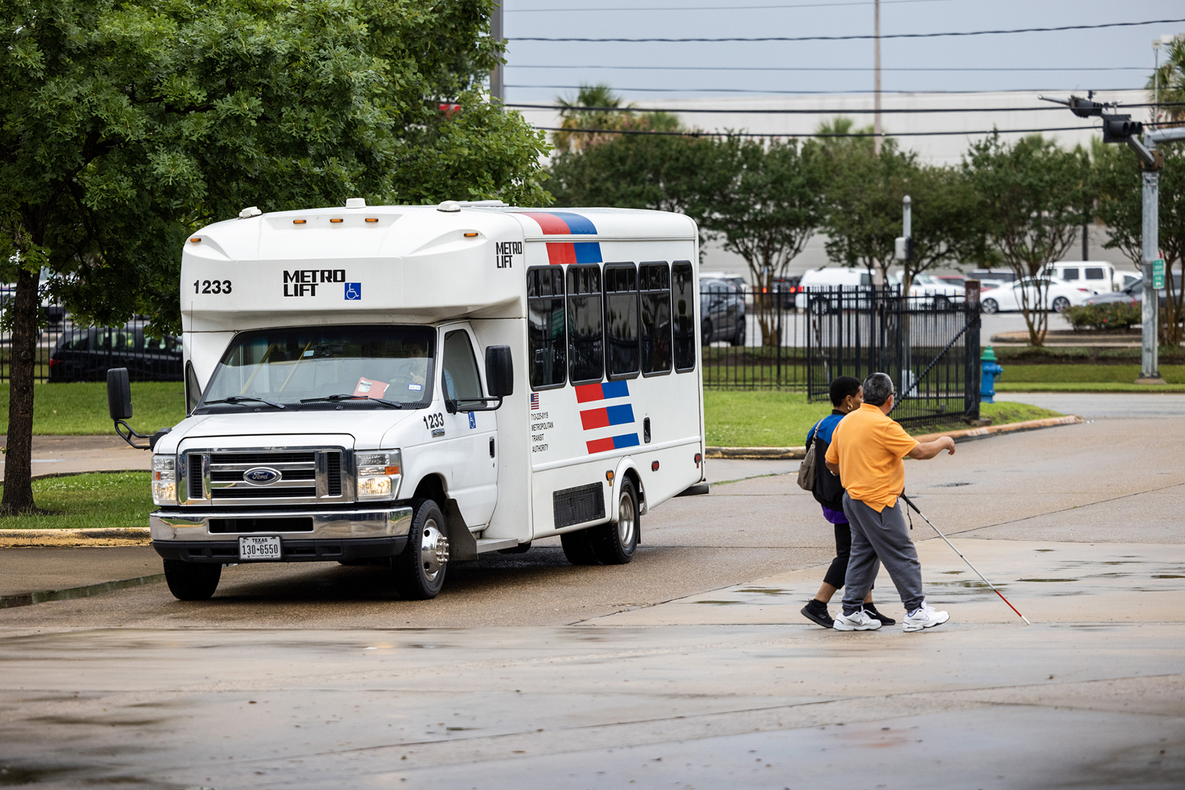 A person with limited vision is aided by a man as a METROLift bus passes by while driving towards Metropolitan Multi-Service Center,