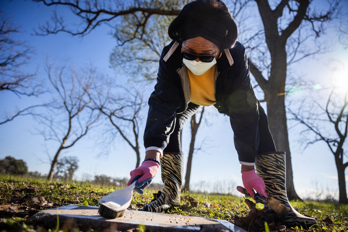 Sharon Harris, a former member of the Fort Bend Historical Commission, brushes dirt off a grave marker at Watts Cemetery