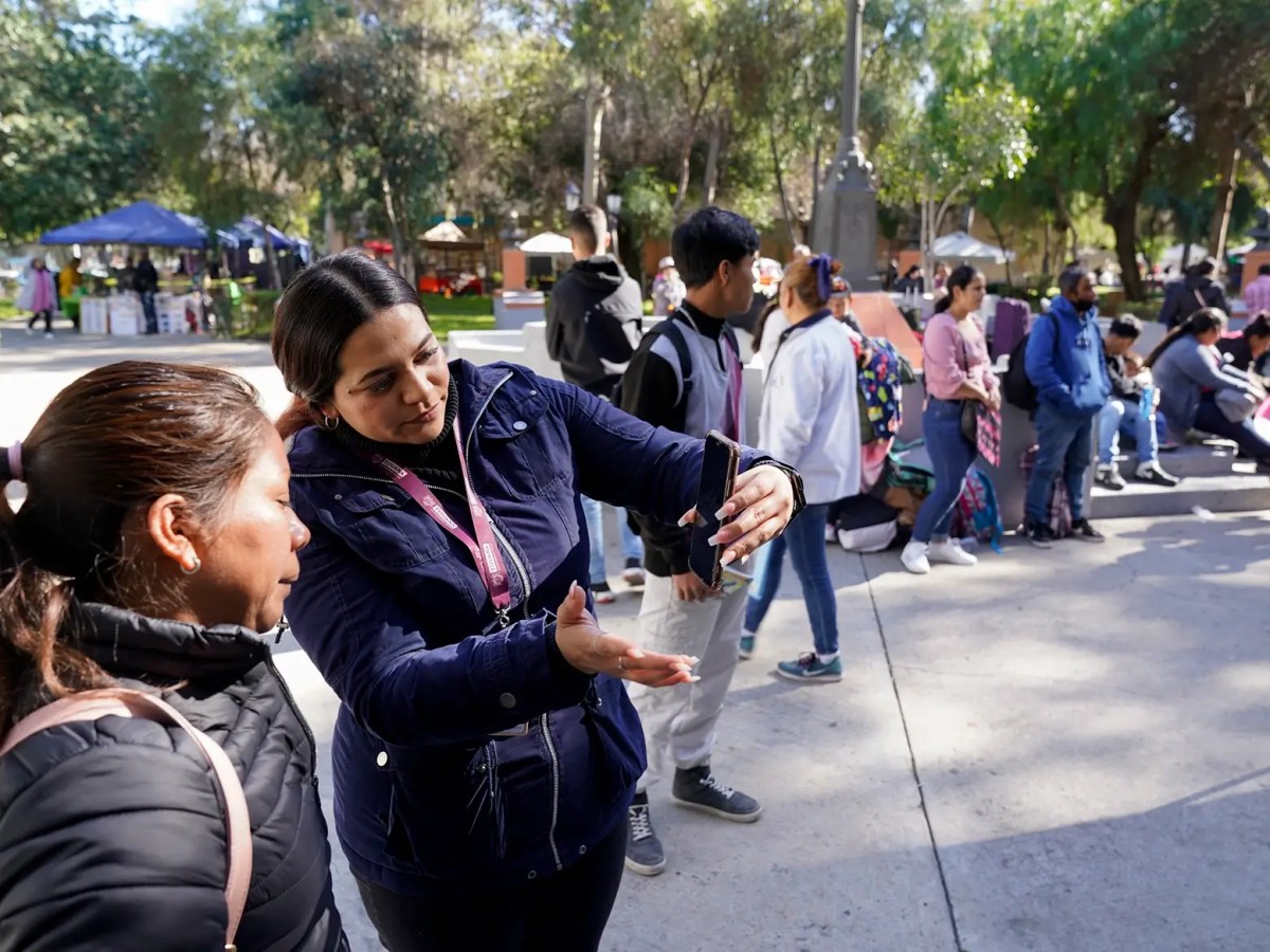 Migrants get help with the CPBOne app from workers in the city of Tijuana, Mexico Tuesday, Jan. 24, 2023, in Tijuana, Mexico. A mobile app for migrants to seek asylum in the United States has been oversaturated since it was introduced this month in one of several major changes to the government's response to unprecedented migration flows.