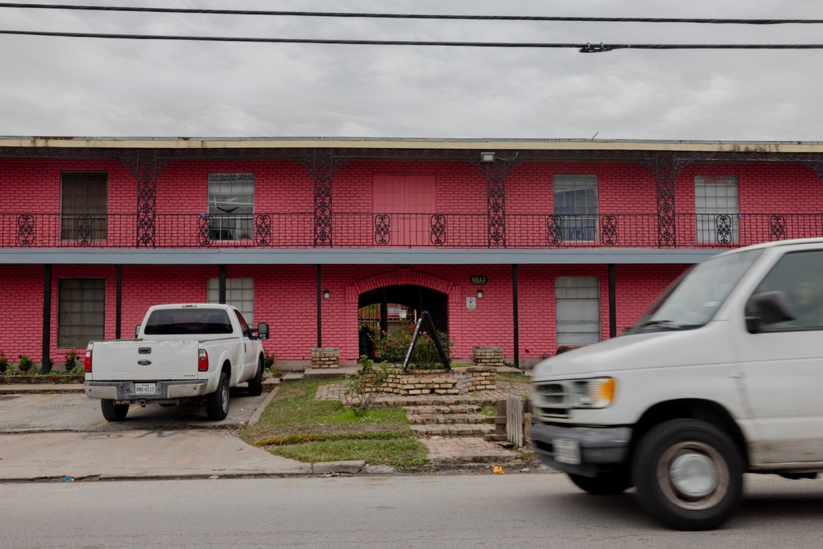 A red, two-story apartment building with a white pick up truck and a white van parked in front.