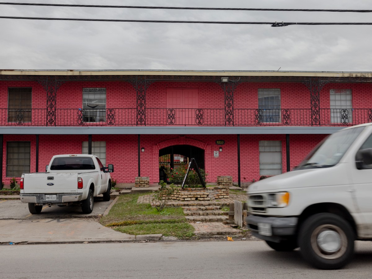 A red, two-story apartment building with a white pick up truck and a white van parked in front.